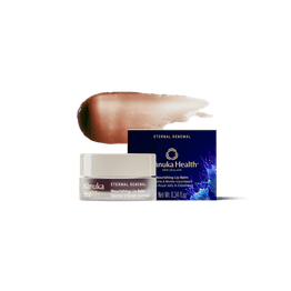 A jar of Manuka Health Eternal Renewal Nourishing Lip Balm with its navy blue box and a brown-to-beige product swatch behind it, set against a solid white background.