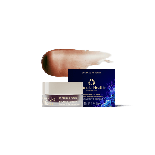 A jar of Manuka Health Eternal Renewal Nourishing Lip Balm with its navy blue box and a brown-to-beige product swatch behind it, set against a solid white background.
