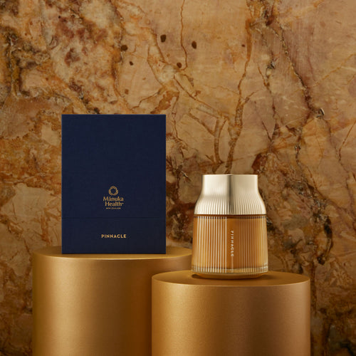 Manuka Honey Pinnacle Harvest MGO 1600+. Decorative vase and box on gold stands against a textured stone wall.